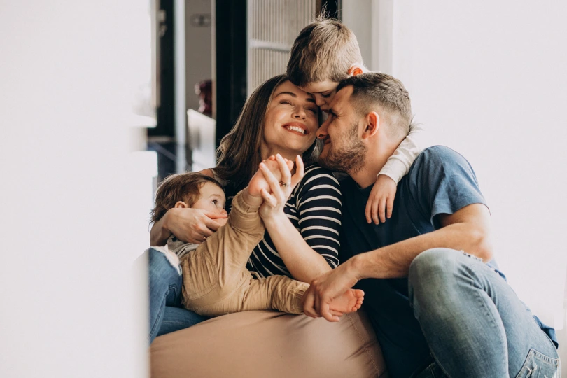 Smiling couple sitting together with two young children cuddling and kissing, a family moment for men considering if they are ready for a vasectomy.
