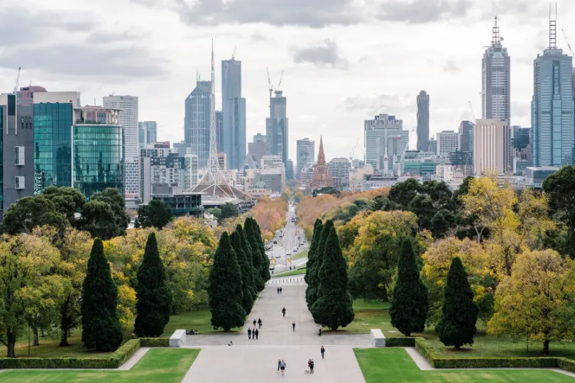 Melbourne CBD skyline viewed from Shrine of Remembrance gardens with cypress trees and pedestrians — vasectomy clinic in Melbourne.